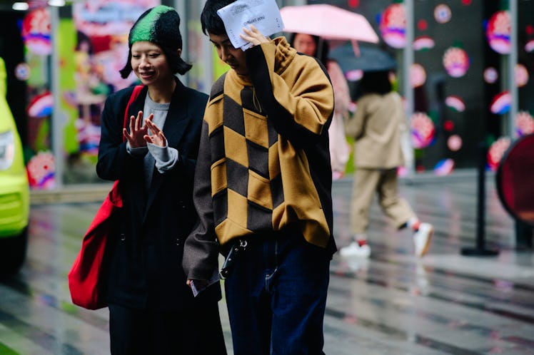 A man and a woman crossing a street together while rain is falling