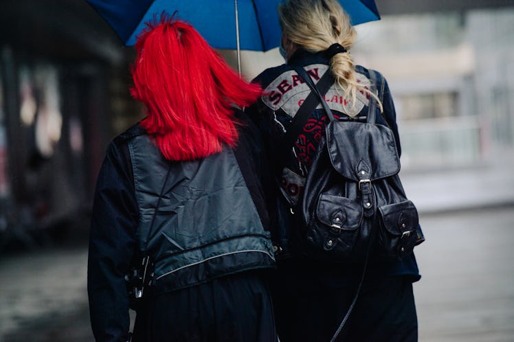 Two women walking under a blue umbrella while wearing black jackets