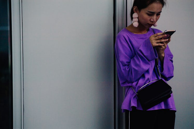 A woman using her phone while wearing a purple blouse
