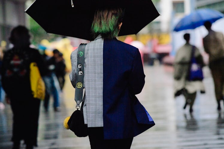 A woman walking down a street while wearing a blue blazer and carrying an umbrella