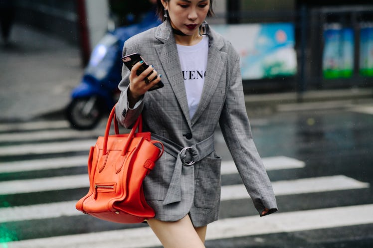 A woman crossing a street while wearing a grey blazer and a white shirt