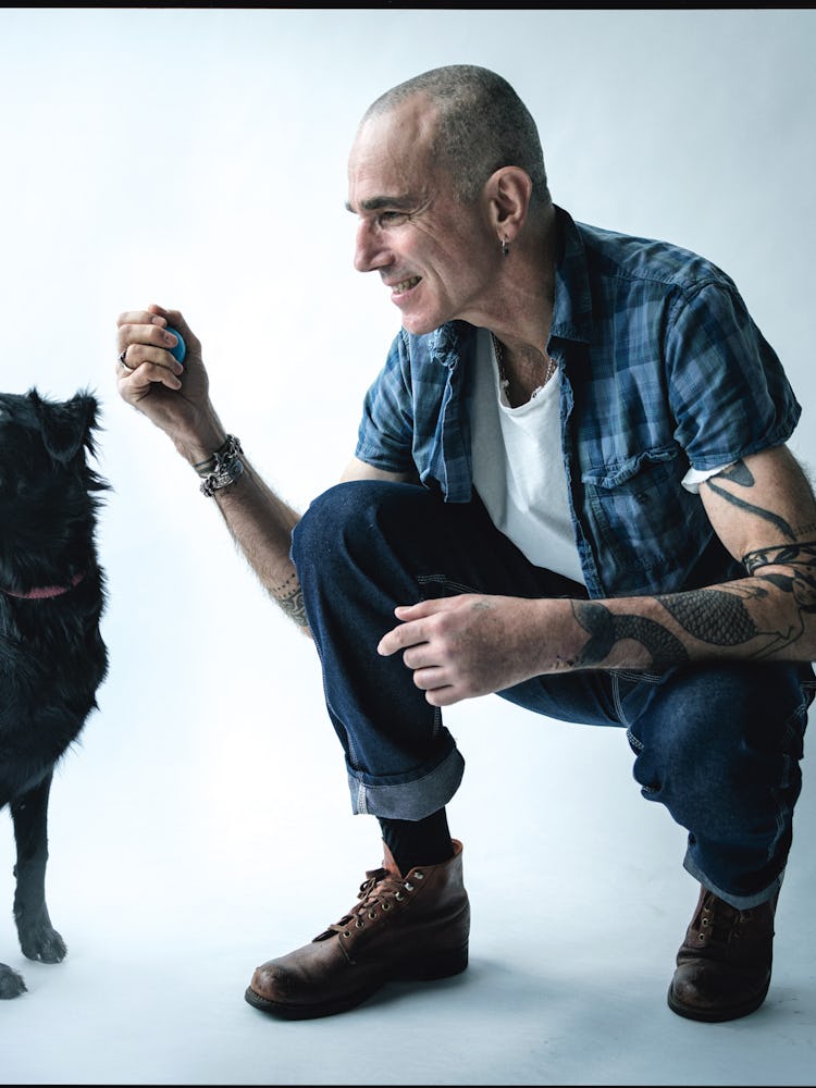 Daniel Day-Lewis smiling and squatting while petting a black dog