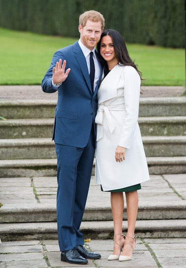 Meghan Markle in a white coat and beige heels standing next to Prince Harry in a blue suit