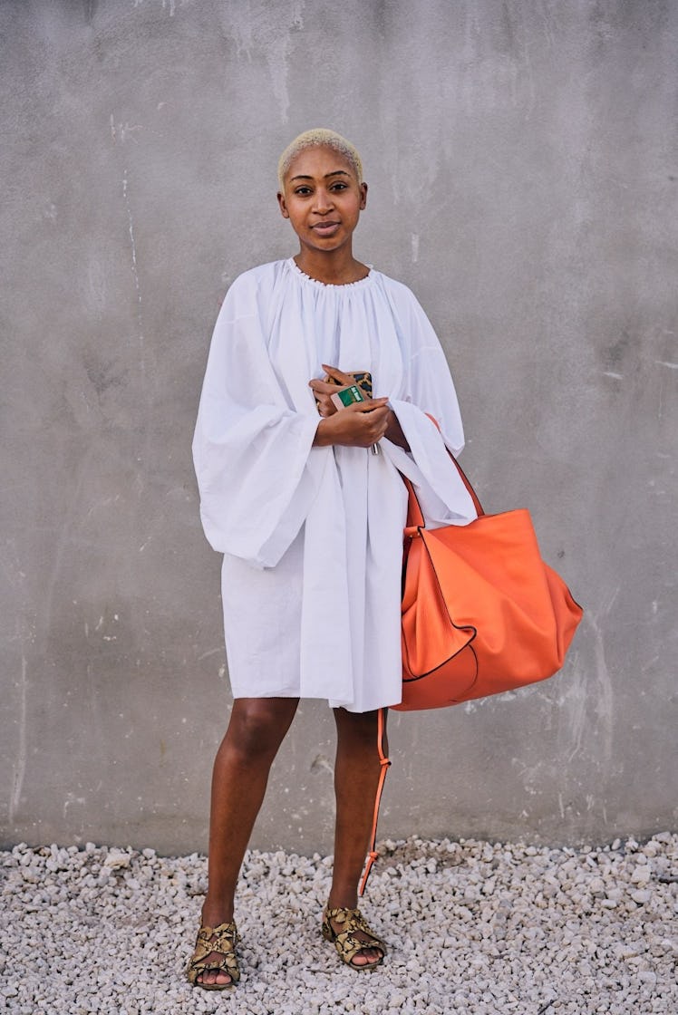 A woman with short blonde hair, wearing a white dress paired with an orange bag at Art Basel Miami i...
