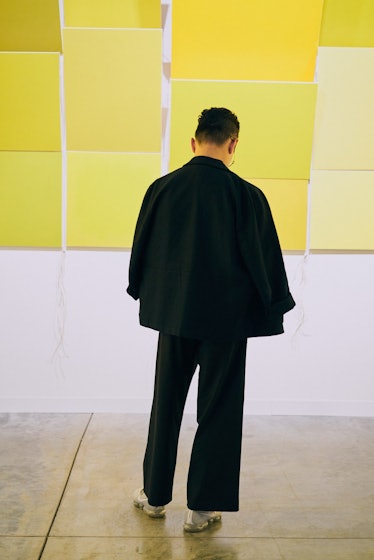A man wearing a black suit posing in front of a yellow wall at Art Basel Miami international art fai...