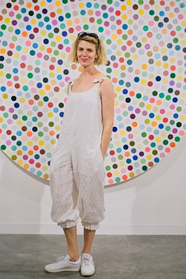 A blonde woman wearing a white jumpsuit posing in front of a colorful artwork at Art Basel Miami 