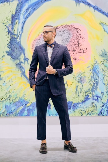 A visitor in a dark blue striped suit posing in front of a colorful wall at Art Basel Miami internat...