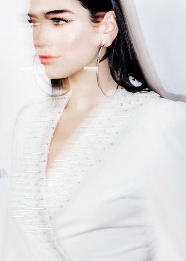 A blurred side-profile portrait of Dua Lipa in a white blazer and large hoop earrings