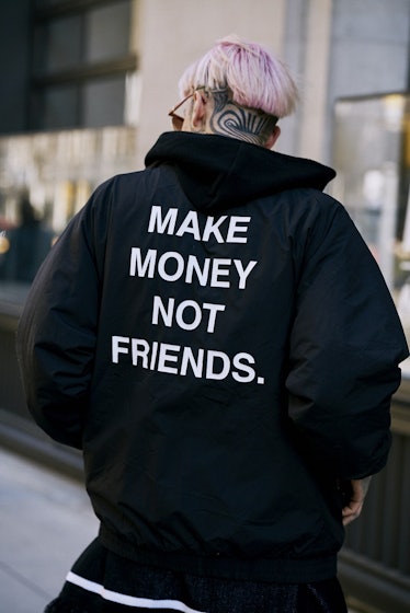 A man wearing a hoodie with a "make money not friends" text sign