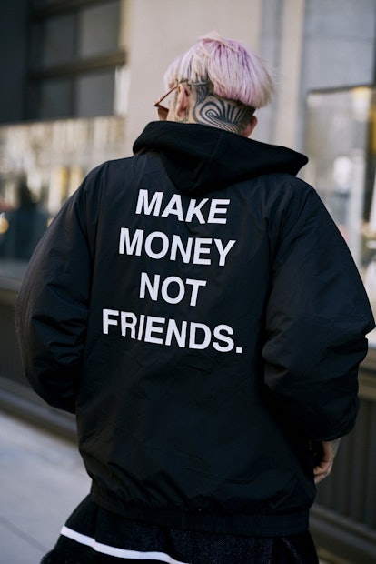 A man from behind with pink hair and a "make money not friends" jacket 
