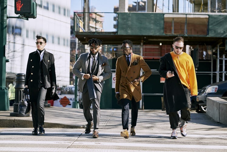 Four men walking in blazers and coats down a street 