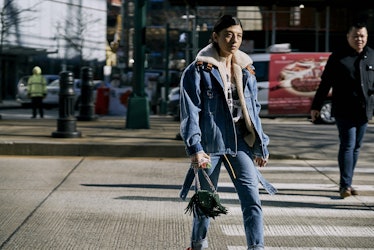 A woman walking in a denim Texas jacket and in denim pants down a street with a black handbag 