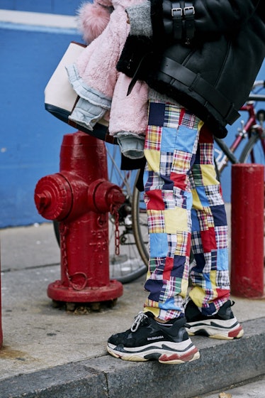 A model standing in the middle of a street and wearing colorful plaid pants