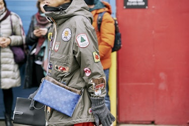 Aman walking in a grey jacket with many logos attached to it 