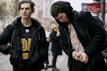 Two boys standing on a street while wearing black jackets