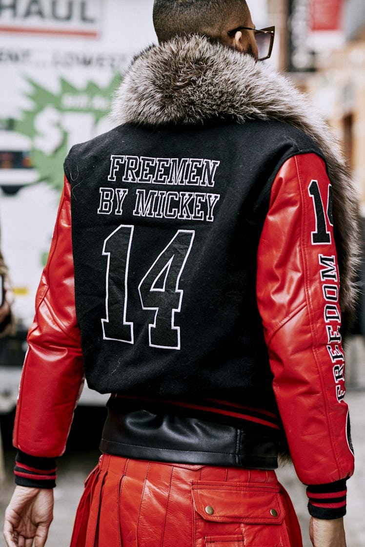 A man walking in a red and black jacket with a "FREEMEN BY MICKEY 14" text sign