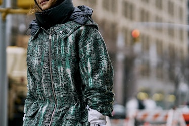 A woman walking at a street while wearing a green coat jacket 