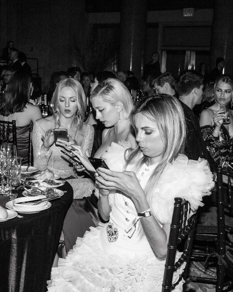 Three female guests sitting and using their phones at the 2018 amfAR Gala