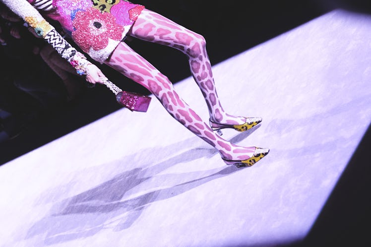 A female model standing in a pink mini dress and pink snake leggings 