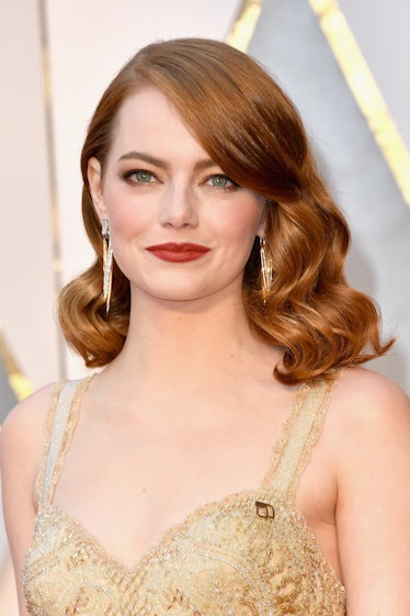 Emma Stone in a golden dress, with her hair slicked back on one side and red lipstick at the Oscars 