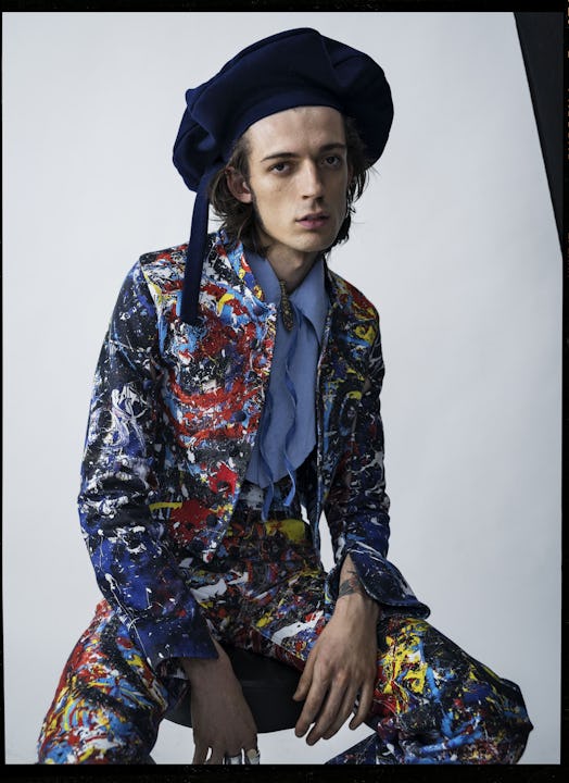 Niall Underwood in a spray-paint multi-colored suit, a blue shirt and a black hat