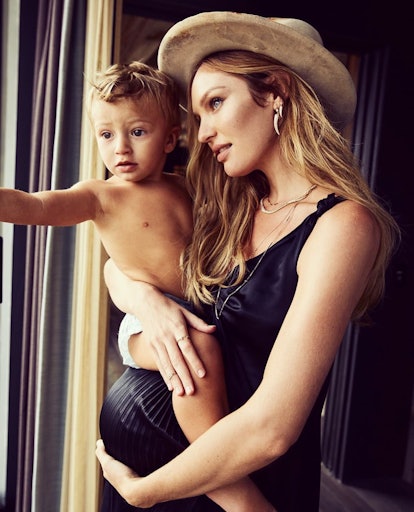 Pregnant mom supermodel Candice Swanepoel looking through the window while holding son.