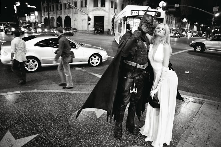 A blonde model in a white dress posing next to a man wearing a Batman costume 