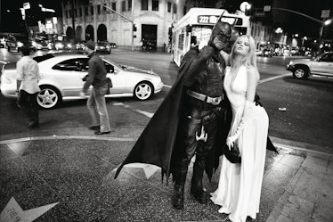 A blonde model in a white dress posing next to a man wearing a Batman costume 