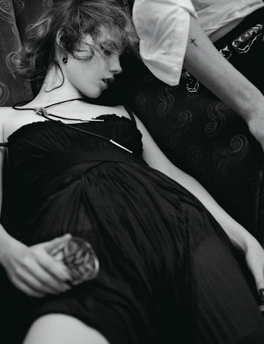A woman in a black dress sleeping with a glass in her hand.