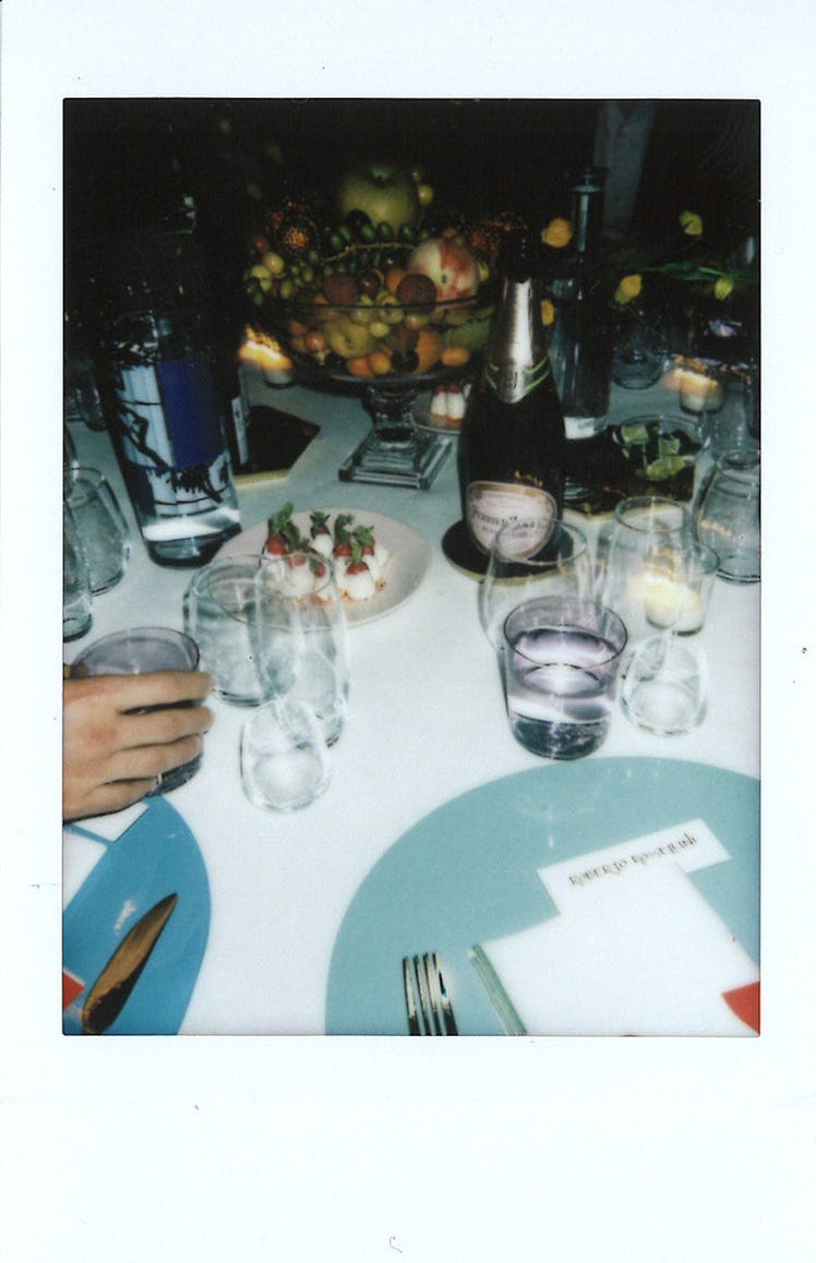 A white table with plates, glasses, drinks and fruits