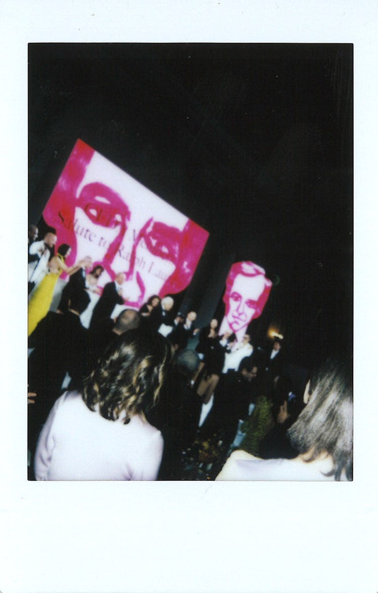 A large crowd in a dark room and pink illustrated man's face on large screens