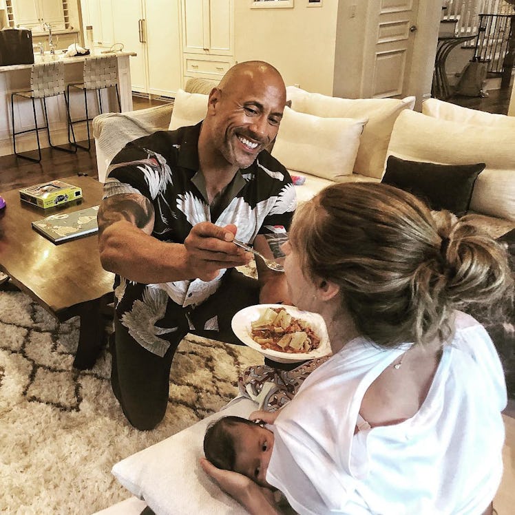 An Instagram post with Dwayne Johnson kneeling and smiling while feeding his wife, who is nursing he...