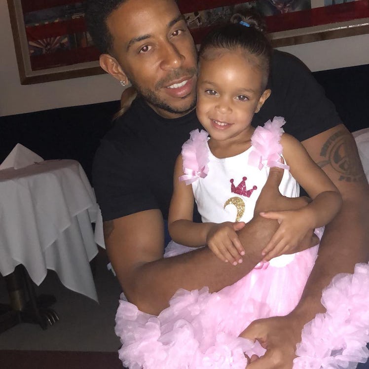 An Instagram post with Ludacris siting in a black shirt and holding his daughter in a pink dress in ...