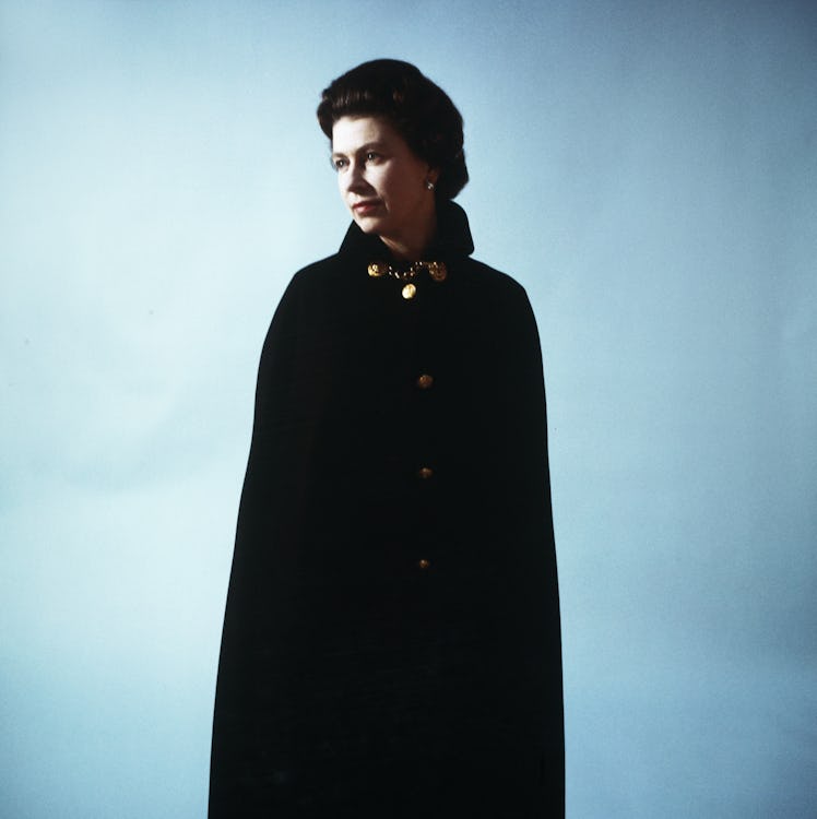 Queen Elizabeth II wearing a black coat in front of a blue background photographed by Cecil Beaton