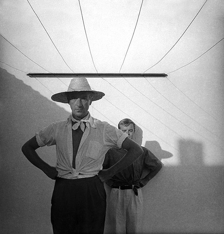 Truman Capote standing in front of a man and under strings photographed by Cecil Beaton