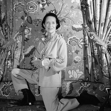 Diana Vreeland kneeling on a couch with her arms crossed, photographed by Cecil Beaton