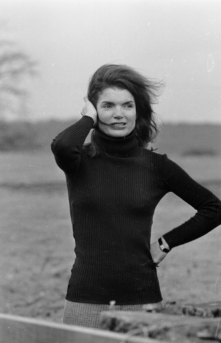 Jackie O looking windswept in a casual black turtleneck wearing a classic small watch with a black l...