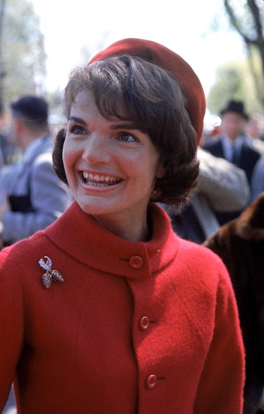 Jackie Kennedy wearing a red jacket with an acorn pin and a red hat. 
