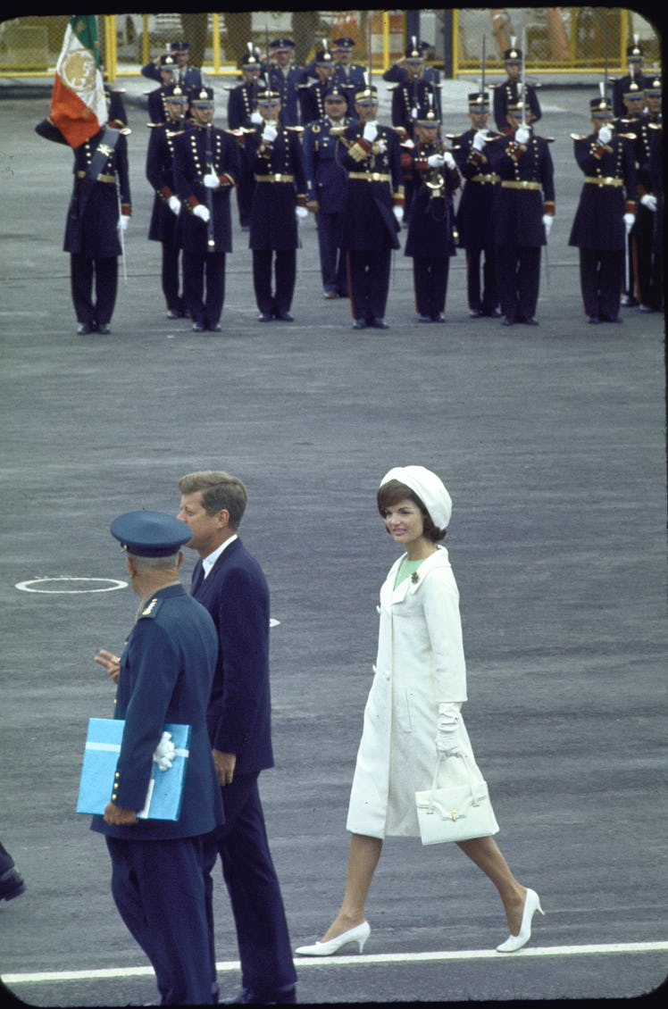 Jackie O wearing a white monochromatic set consisting of a dress, coat, shoes, hat and bag.