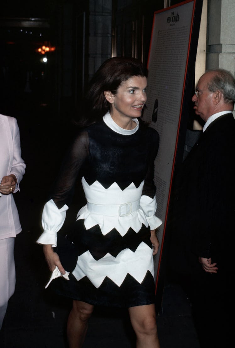 Jackie O in a black cocktail dress with white geometric inserts, bringing it all together with a sta...