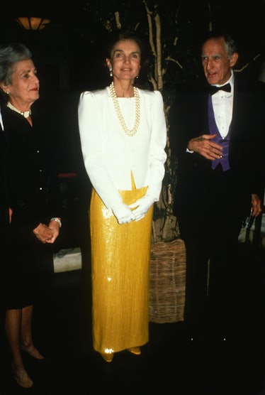 Jackie Kennedy at an event in New York wearing a white blazer and yellow sequined dress, with a whit...