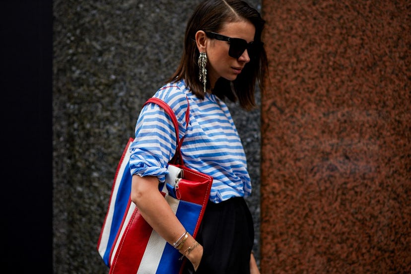 A woman wearing French girl-approved pieces: a blue-white striped shirt, a blue-white-red bag and bl...