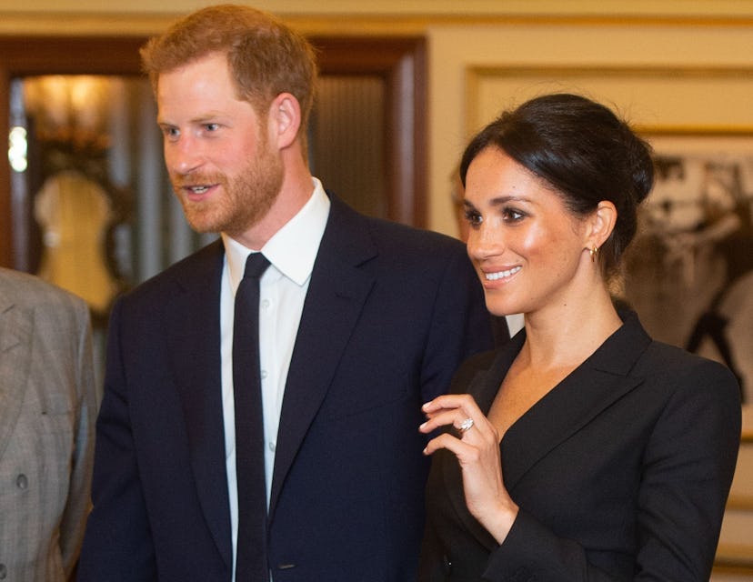 Meghan Markle wearing a black tuxedo dress while standing next to Prince Harry
