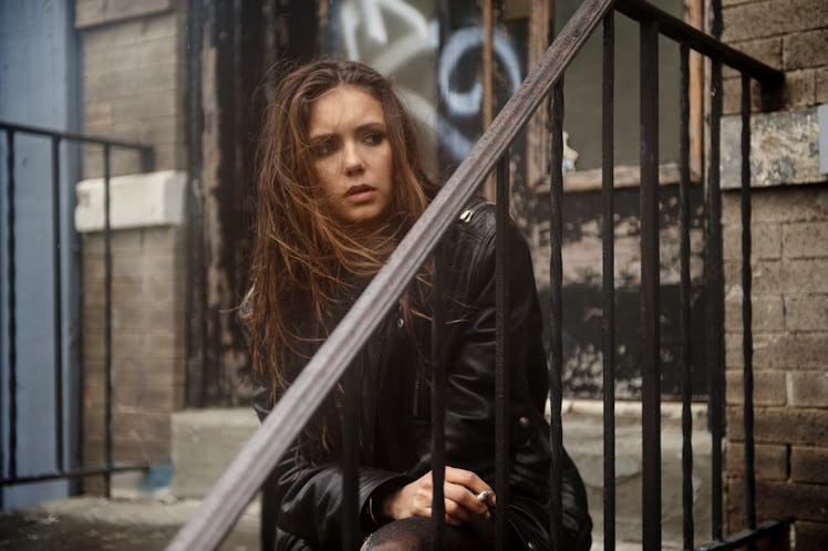 Nina Dobrev sitting on stairs while wearing a black jacket