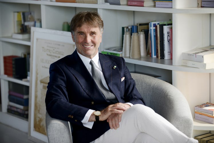 Brunello Cucinelli sitting in his armchair wearing an elegant navy-blue blazer and white pants combi...