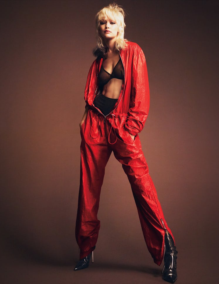 Gigi Hadid posing while wearing a black bra, black underpants, and a red tracksuit