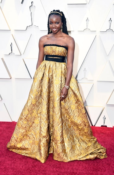 Danai Gurira wearing a long black-and-gold gown while attending the 2019 Oscars Red carpet 