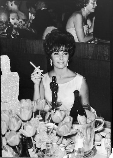 Actress Elizabeth Taylor at Hollywood party after winning oscar, which is on table in front of her.