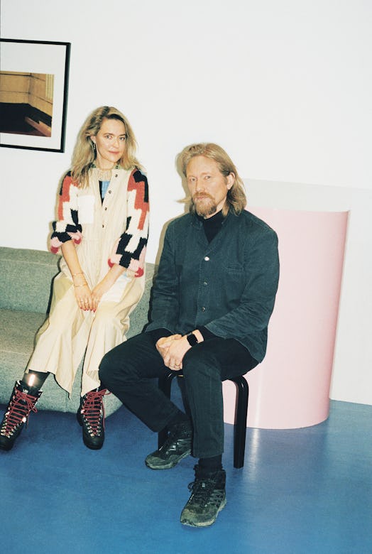 Ditte in a beige-orange-black dress sitting on a couch and Nicolaj Reffstrup sitting on a chair in a...