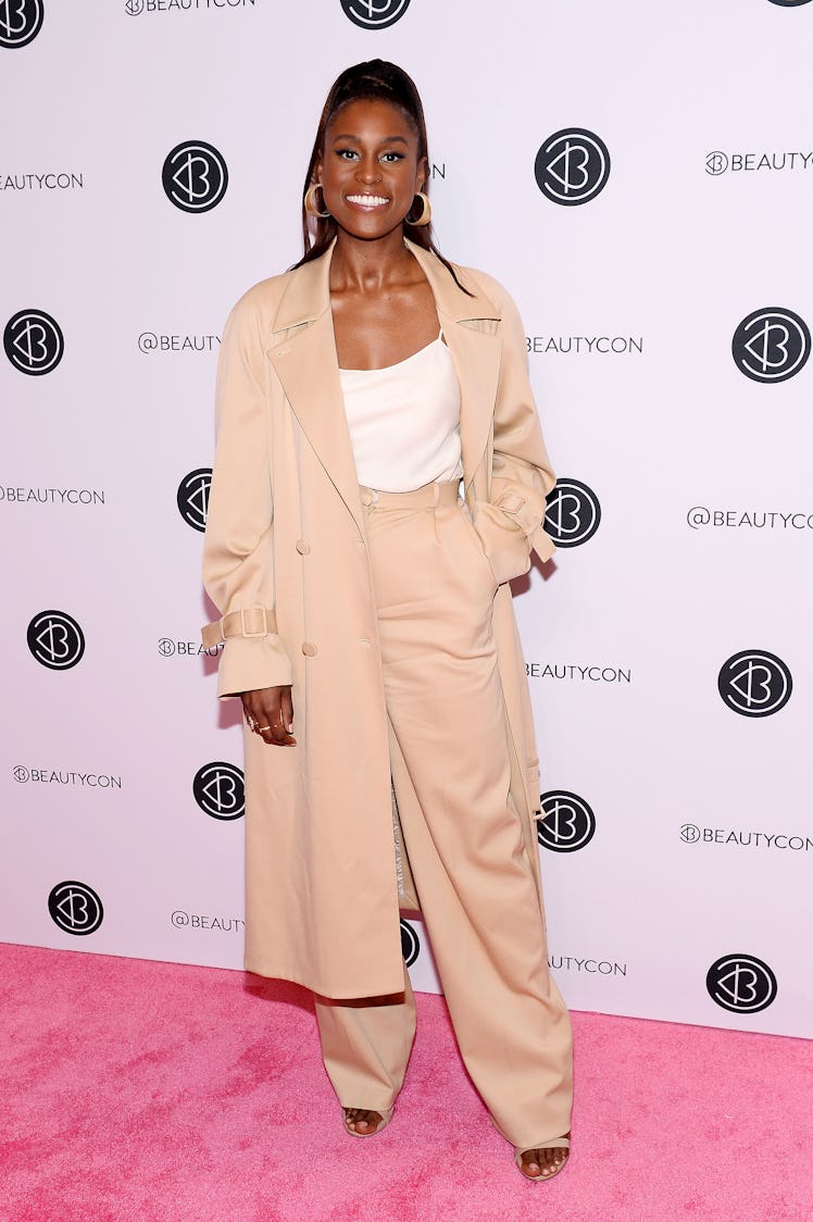 Issa Rae wearing an oversized tan suit with a white shirt underneath, sporting a high ponytail